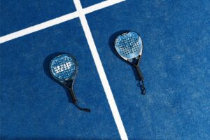 Two padel players in action, expertly hitting the ball with their rackets and pala on a professional padel court, showcasing the excitement and strategy of the sport in a blog post about padel tips and techniques.